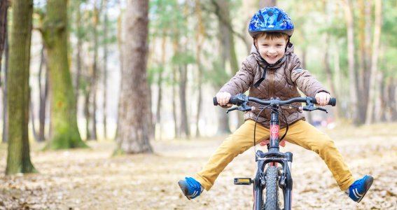 Ein Kind fährt Fahrrad im Wald und streckt seine Beine aus.