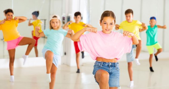 Mehrere Kinder in bunten Outfits tanzen in einem Raum mit Spiegelwand