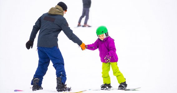 Kind lernt mit Snowboardlehrer die Piste herunterzufahren 