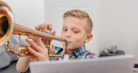Junge spielt Trompete und schaut auf Laptop