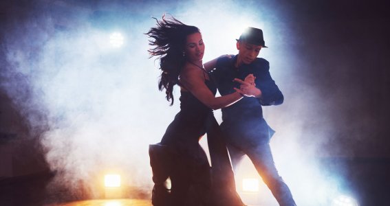 Ein junges Paar in schicker Kleidung tanzt im Scheinwerferlicht mit Nebeleffekt