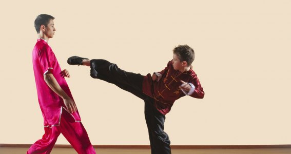 Ein Junge übt eine Tritttechnik mit einem Jugendlichen in Kung Fu Kleidung