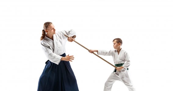 Ein Mann in japanischer Kampfkunstkleidung trainiert Kampfsport mit einem Jungen mit einem Holzstock