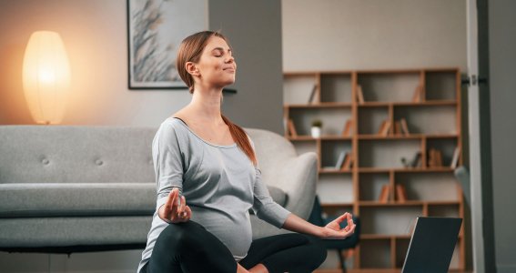 Eine schwangere Frau meditiert auf einer Yogamatte vor einer Couch