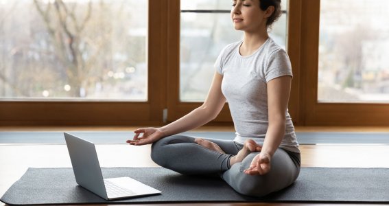 Eine meditierende Frau auf einer Yogamatte vor einer Fensterwand