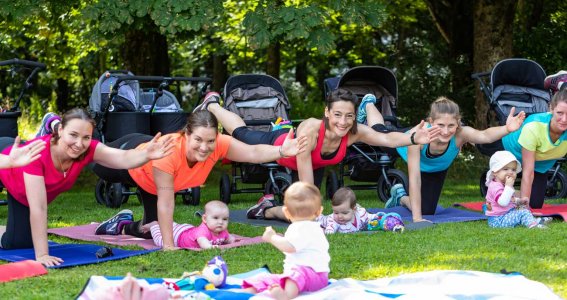 Mamas machen Fitnessübungen im Park, die Kinder spielen